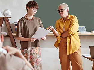 Eine Lehrerin zeigt auf das Aufgabenblatt ihrer Schülerin 