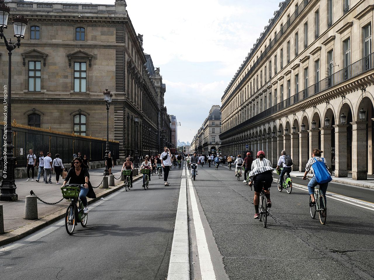 Auf einer breiten Straße in Paris fahren viele Radfahrer*innen