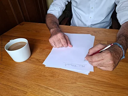 Eine Person sitzt am Tisch und setzt ein Schriftstück auf.