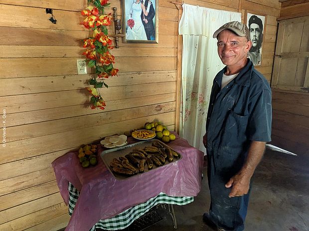 Ein Landwirt aus der Projektregion steht in einem einfachen Holzhaus neben einem Tisch mit Obst und Essen. © OroVerde - K. Osen
