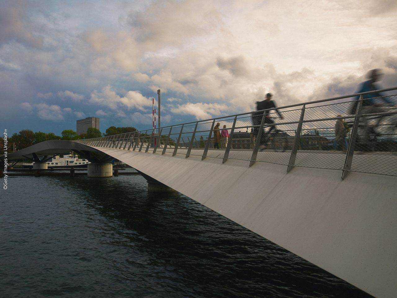 Eine Fahrradbrücke über einem Fluss in Kopenhagen. Zwei Radfahrer*innen fahren gerade auf der Brücke und aus dem Bild heraus.