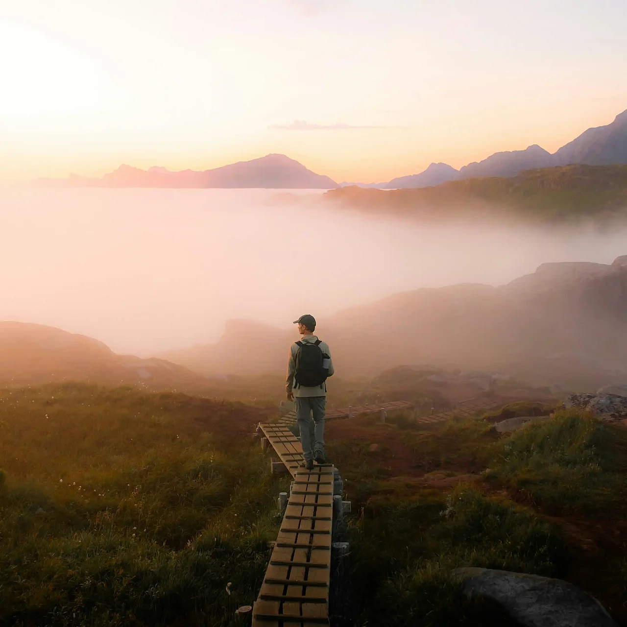 Wanderer auf Holzpfad in nebliger Berglandschaft bei Sonnenaufgang