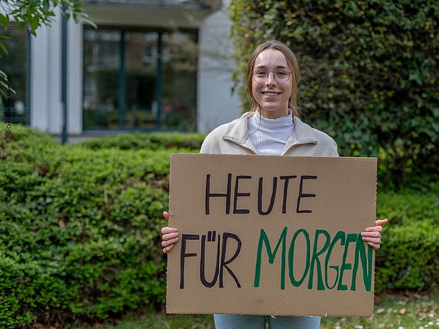Eine Bufdi hält ein Schild in die Kamera. Darauf steht: "Heute für morgen."