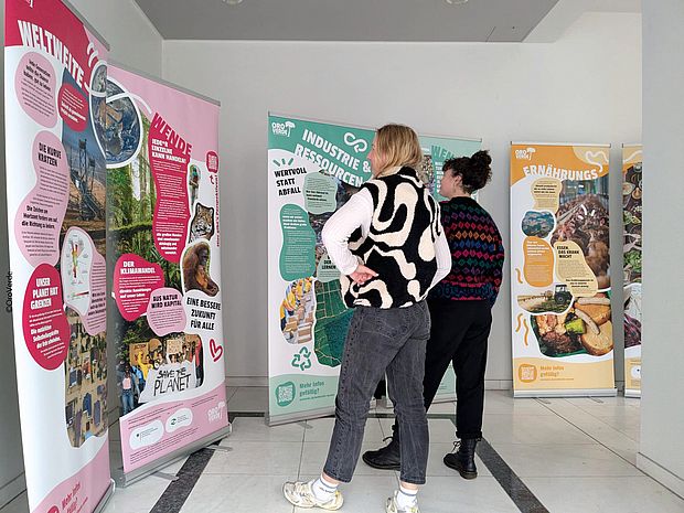 Zwei Personen schauen sich in einer Ausstellung OroVerde-Plakate an.