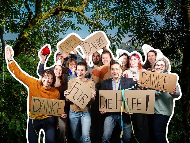 Feiernde Menschen mit Danke-Schildern vor einem Regenwald