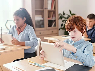 Drei Schüler*innen sitzen mit Tablet in der Schulklasse