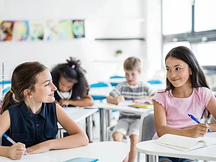 Vier Schüler*innen sitzen in einem Klassenzimmer und gehen ihren Aufgaben nach