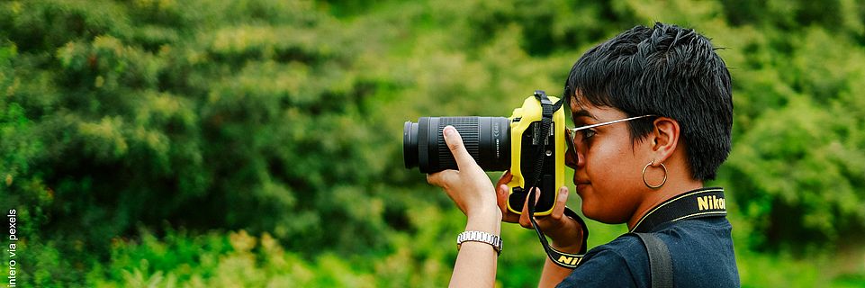 Seitenansicht einer jungen Frau, die mit einer DSLR-Kamera ein Bild in der Natur macht.