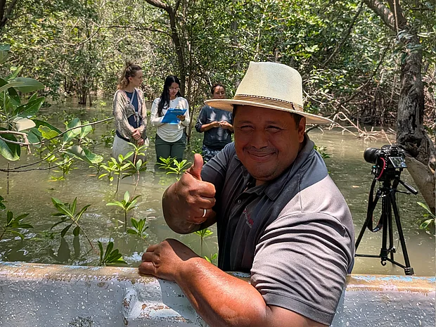 Fischer Franklin Ovet Gomez Quevedo zeigt vor Mangroven im Wasser Daumen hoch in die Kamera. 