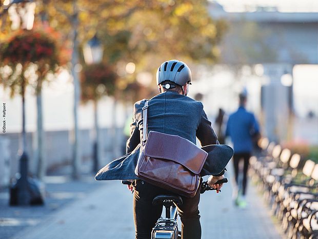 Ein Mann auf dem Fahrrad von hinten mit Helm und Tasche auf dem Weg zur Arbeit