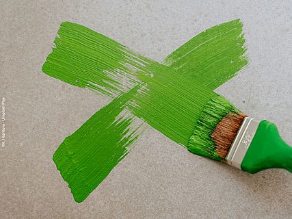 Auf eine Wand wird mit grüner Farbe ein X gemalt